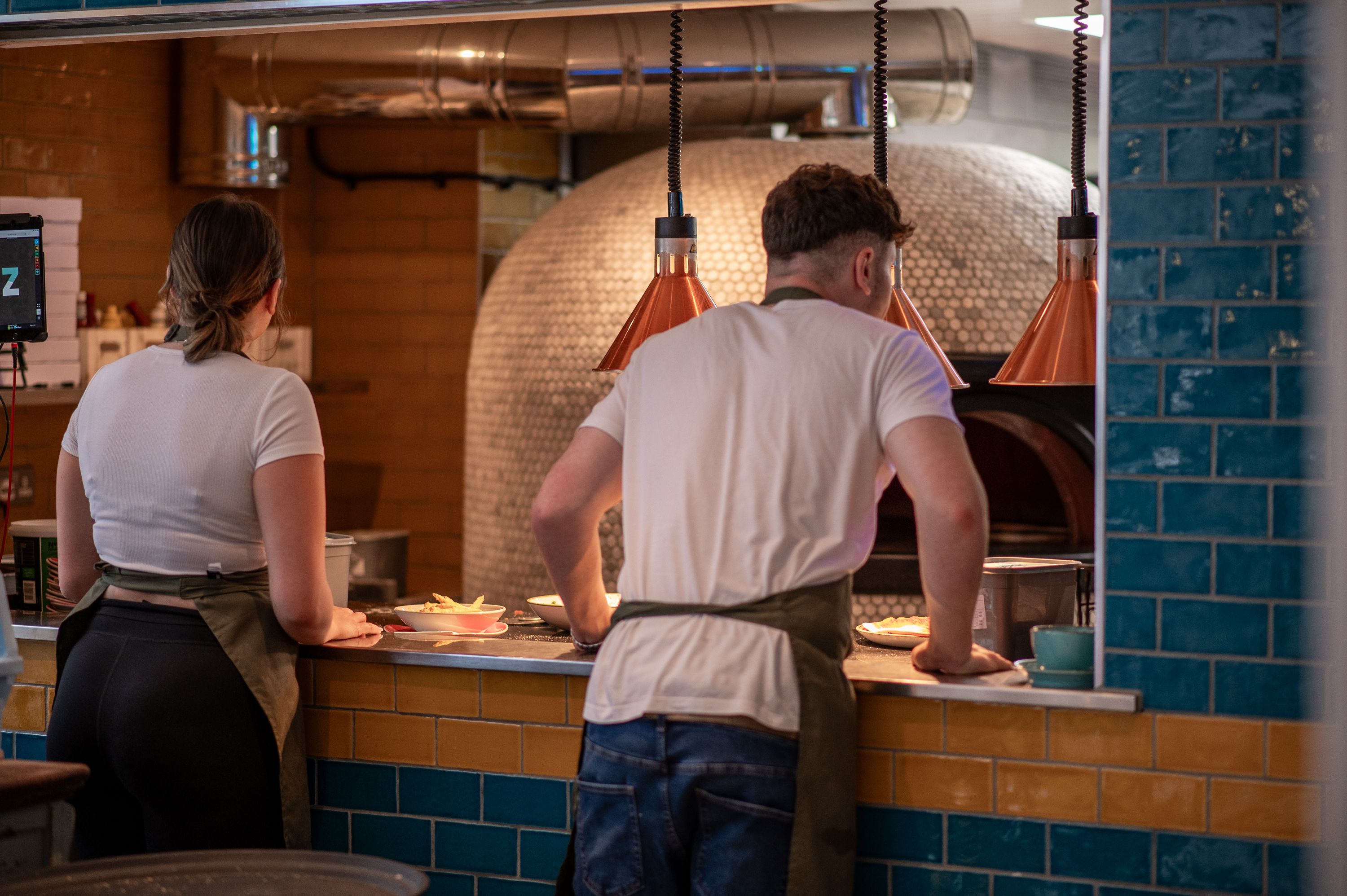Male and female waiters waiting at open kitchen to serve food
